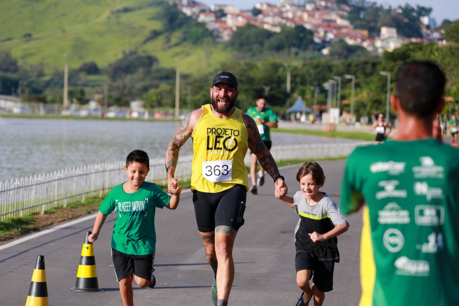 Corredor com duas crianças de mãos dadas em prova de rua na margem do lago do parque