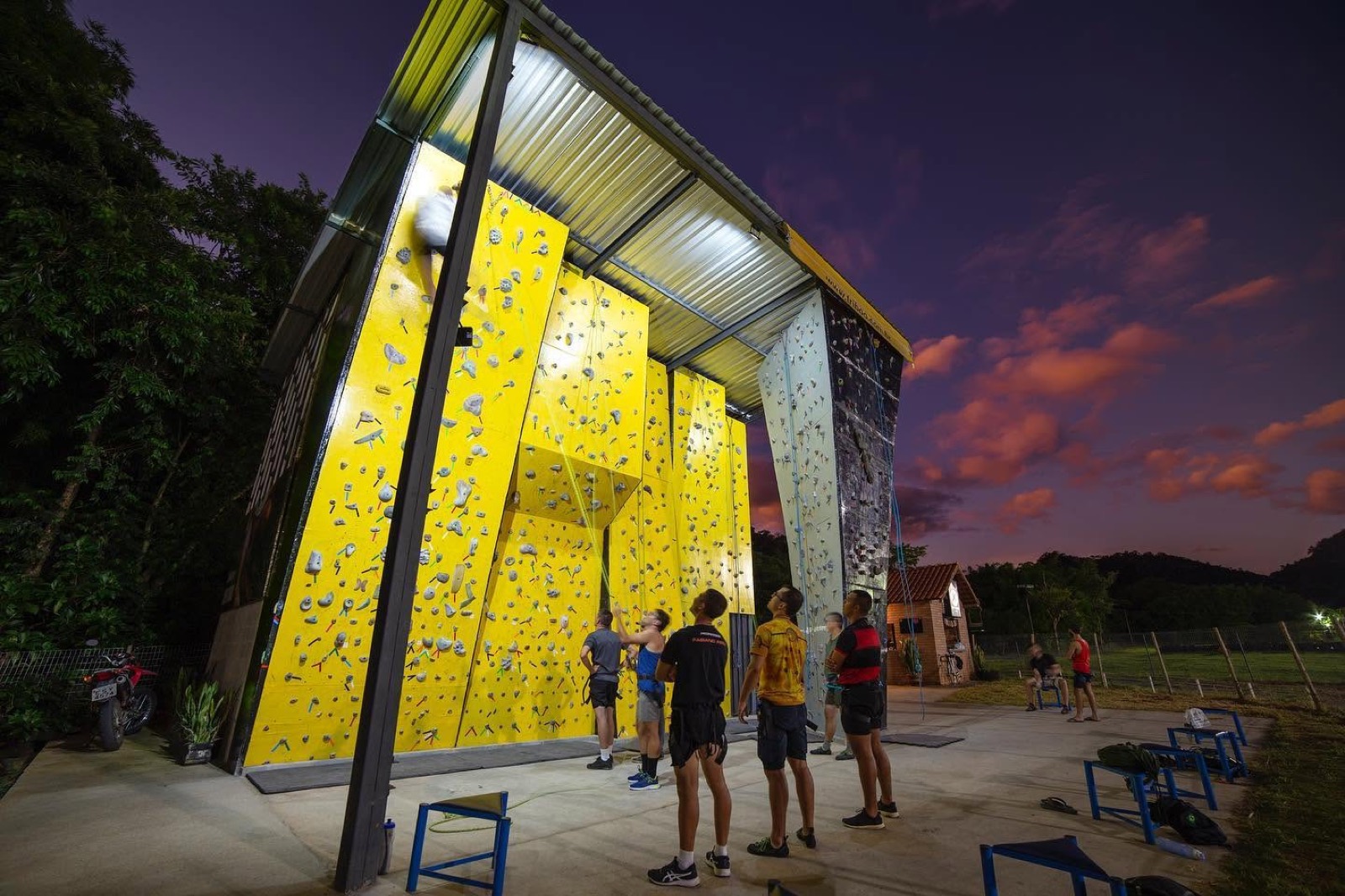 Parede de escalada iluminada do Parque da Cidade de Itajubá ao entardecer, com escaladores no muro amarelo