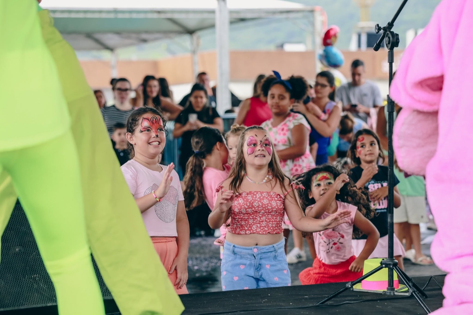 Crianças com pintura no rosto em frente ao palco infantil do parque