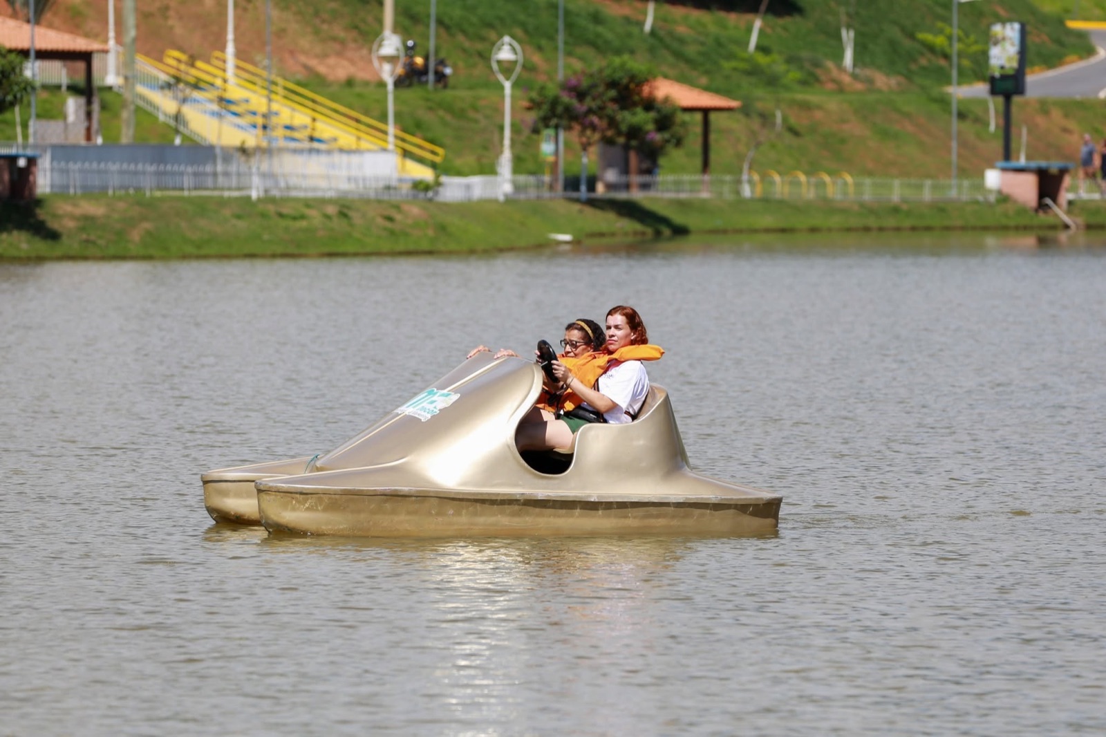 Duas visitantes pilotando pedalinho dourado no lago do parque